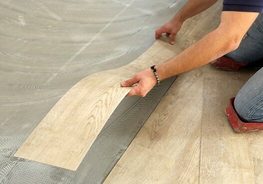 Worker installing new vinyl tile floor | Kay Riley Flooring and Design
